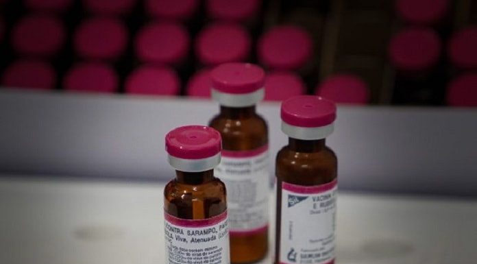 três ampolas de doses de vacina sobre uma bancada e outras organizadas em bandeja ao fundo
