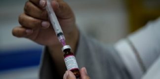 pessoa retira dose de vacina da ampola com uma agulha em seringa