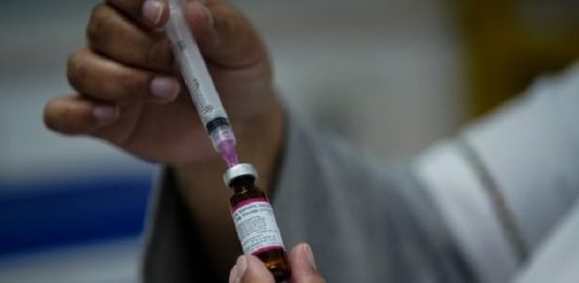 pessoa retira dose de vacina da ampola com uma agulha em seringa