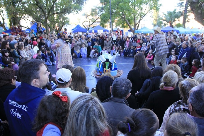 grande público reunido em volta de um pequeno palco ao centro onde há apresentação de boi de mamão