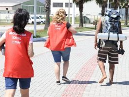 duas agentes com coletes de abordagem social ao lado de andarilho