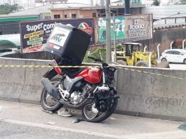 moto com baú batida e amassada apoiada na mureta de concreto da br 101 com uma fita zebrada por cima