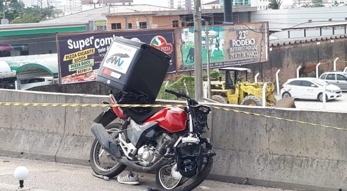 moto com baú batida e amassada apoiada na mureta de concreto da br 101 com uma fita zebrada por cima
