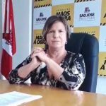 adeliana sentada atrás de uma mesa com painel ao fundo com logos da prefeitura