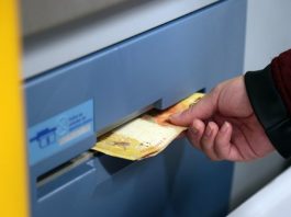 Mão de um homem sacando notas de R$ 20,00 em um caixa eletrônico