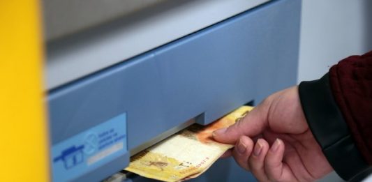 Mão de um homem sacando notas de R$ 20,00 em um caixa eletrônico