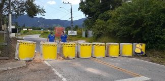barreira em governador celso ramos feita de tubos de concreto amarelas fechando uma rua com homens com máscara atrás