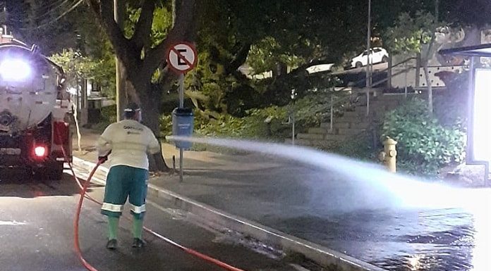 funcionário da comcap lava calçada em frente ao hemosc de noite com grande jato de água