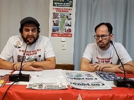 presidente e outro membro do sindicato com camisetas de campanha sentado atrás de mesa com panfletos e com microfones na frente