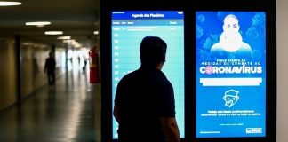 silhueta de um homem em corredor do senado com cartaz luminoso sobre coronavírus