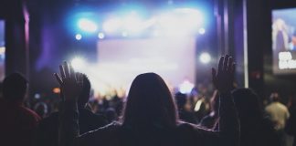 silhueta de mulher com braços levantados em meio à multidão em culto
