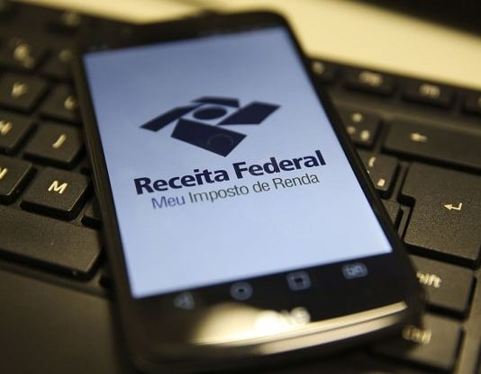celular com logo da receita federal ocupando toda tela sobre teclado de computador