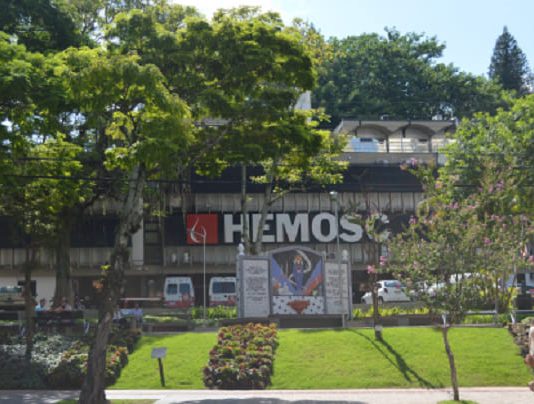 Hemosc pede que pessoas saudáveis permaneçam doando sangue frente do prédio do hemosc em florianópolis com muitas árvores na frente