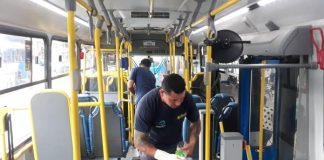 dois homens com luvas e alcool gel fazem limpeza dentro de ônibus