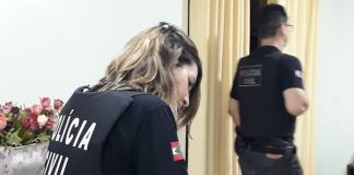 agente mulher da polícia civil com coleta à prova de balas com inscrição da pc escrevendo em prancheta sobre balcão