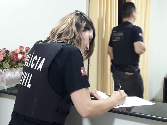 agente mulher da polícia civil com coleta à prova de balas com inscrição da pc escrevendo em prancheta sobre balcão