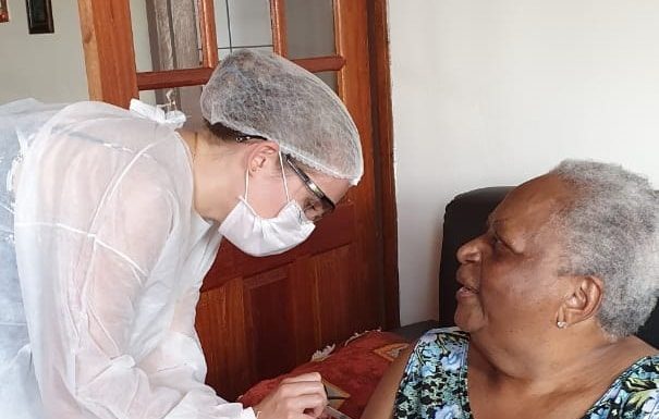 profissional de saúde trajando epi aplica vacina no braço da idosa sentada