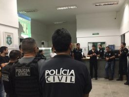 Quadrilha que dava golpes em SC, PI e ES é desarticulada na Operação Precatório policiais civis reunidos em um hall conversando em pé; em primeiro plano agente de costas para foto com inscrição "polícia civil" nas costas