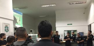 policiais civis reunidos em um hall conversando em pé; em primeiro plano agente de costas para foto com inscrição "polícia civil" nas costas