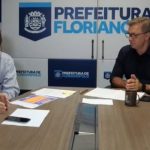 secretário e prefeito sentados na ponta de mesa com painel ao fundo com logos da prefeitura