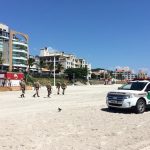 carro ford edge da pm na faixa de areia de canasvieiras com cinco policiais andando e prédios ao fundo