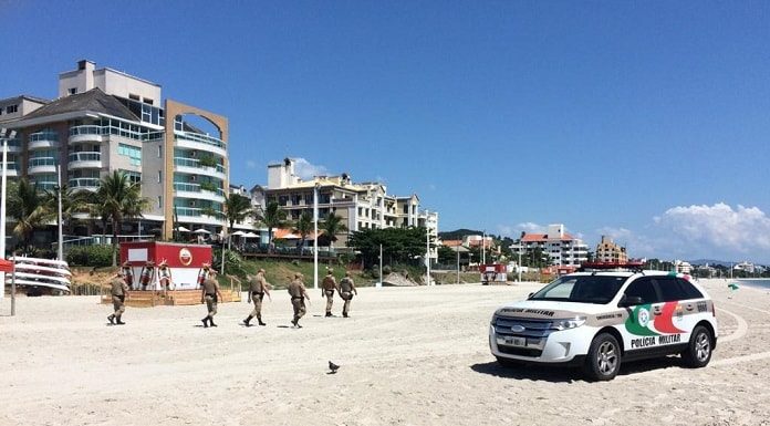 carro ford edge da pm na faixa de areia de canasvieiras com cinco policiais andando e prédios ao fundo
