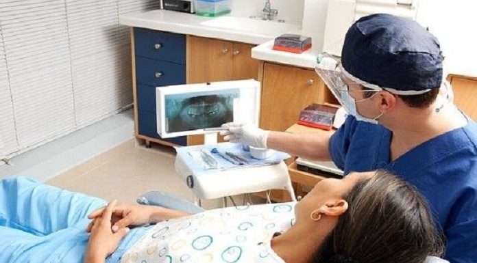mulher em cadeira de dentista, que aponta para raio x dos dentes no consultório