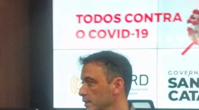 secretário dando entrevista com painel ao fundo escrito covid-19