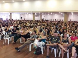 centenas de pessoas sentadas em cadeiras de plástico em grande salão