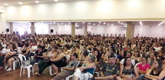 centenas de pessoas sentadas em cadeiras de plástico em grande salão