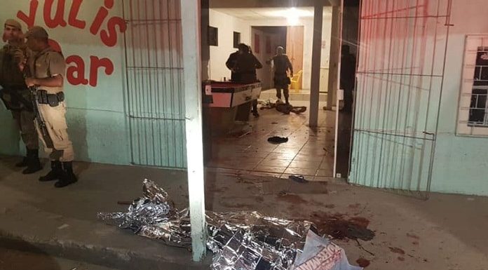 corpo no chão coberto com manta metálica em frente ao bar e alguns policiais em volta