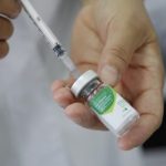 pessoa retira dose de vacina de uma ampola com agulha