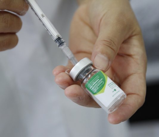 mão com seringa pegando vacina do frasco