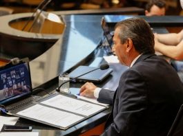 deputado júlio garcia em bancada da alesc com notebook à frente com transmissão dos deputados