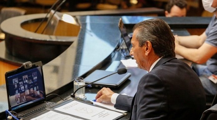 deputado júlio garcia em bancada da alesc com notebook à frente com transmissão dos deputados
