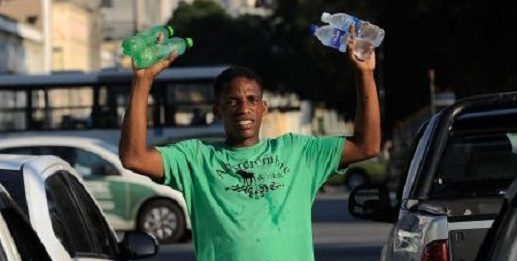 homem segura e levanta quatro garrafas de água na mão no meio de carros