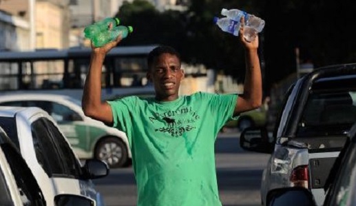 homem segura e levanta quatro garrafas de água na mão no meio de carros