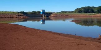 reservatório de água com lamina de água em área de terra, com barragem ao fundo