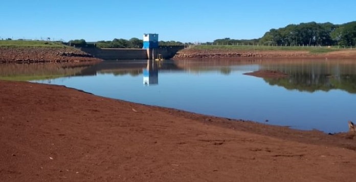 reservatório de água com lamina de água em área de terra, com barragem ao fundo