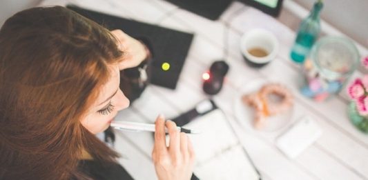 Mais tempo na preparação do vestibular moça vista de cima com caneta na boca em frente à mesa com café e objetos de estudo
