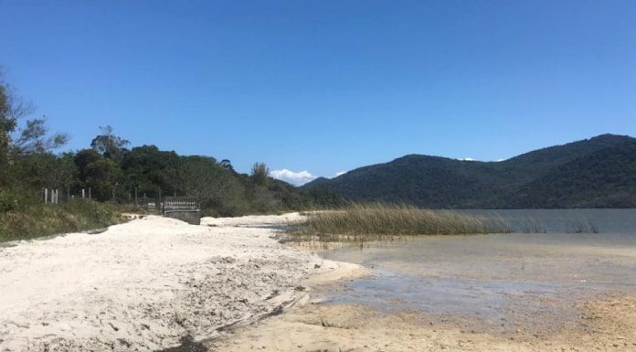 parte de areia na margem da lagoa, com a água no centro da imagem e montanhas ao fundo