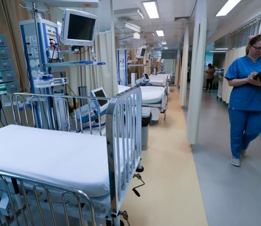 profissional de saúde andando no corredor de uti com leitos expostos pelas cortinas recolhidass