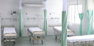 quatro camas de hospital arrumadas e vazias lado a lado, separadas por cortinas recolhidas