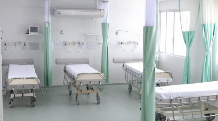 quatro camas de hospital arrumadas e vazias lado a lado, separadas por cortinas recolhidas
