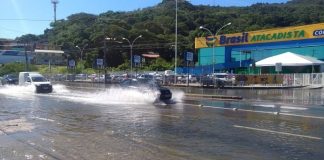 carros passando e espirrando água em rua alagada com loja de supermercado ao fundo