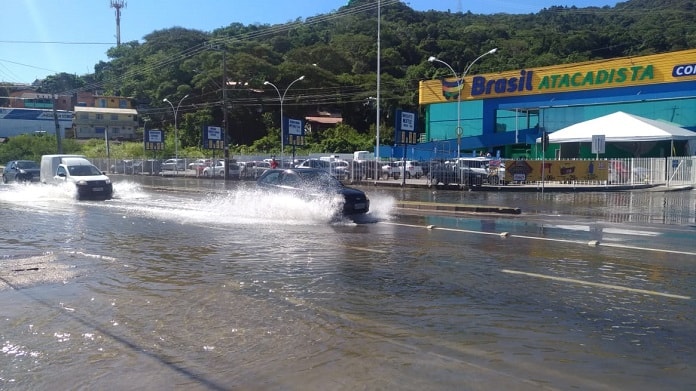 carros passando e espirrando água em rua alagada com loja de supermercado ao fundo