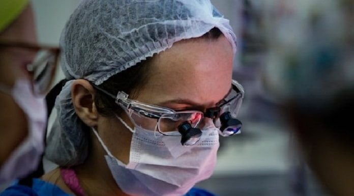 close em rosto de médica com equipamentos de proteção e lupas sobre óculos para cirurgia