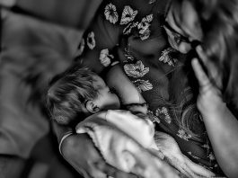 Gestantes e mulheres no pós-parto entram para o grupo de risco da Covid-19 foto em PB de mulher amamentando neném vista de cima no sofá