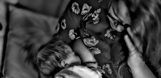 foto em PB de mulher amamentando neném vista de cima no sofá