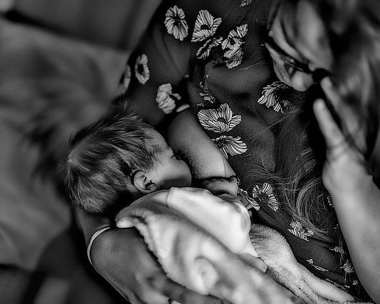 foto em PB de mulher amamentando neném vista de cima no sofá